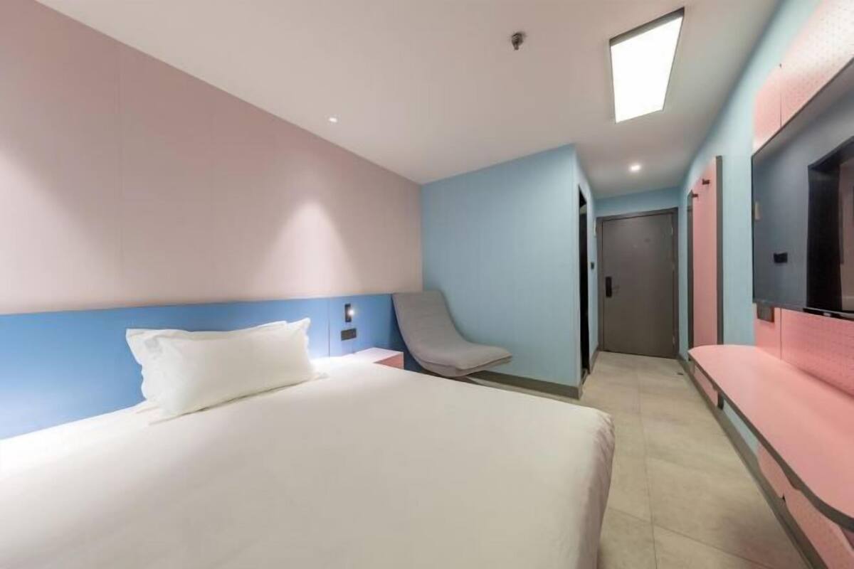 A hotel room with a bed, a chair, a TV, and a door leading to another room.