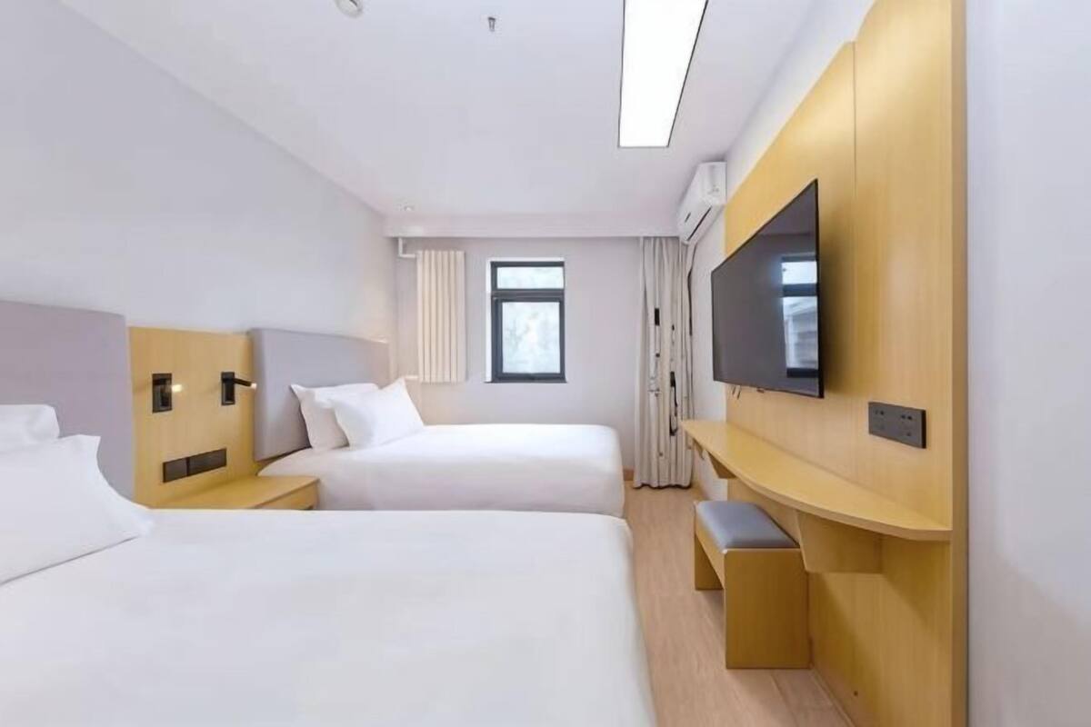 A hotel room with two beds, a TV, a desk, and a window.