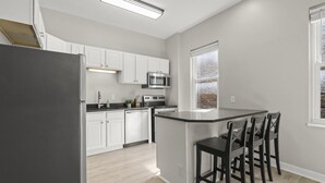 A modern kitchen with white cabinets, a black refrigerator, a microwave, an oven, and a bar area with stools.