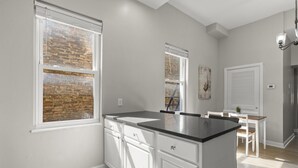 A modern kitchen with white cabinets, a black countertop, and a window with a brick wall view.