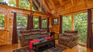 L’intérieur d’un chalet en bois est aménagé avec un ensemble de canapés, une table basse et de grandes fenêtres qui offrent une vue sur la forêt.