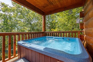 Una terraza de madera con un jacuzzi, rodeada de árboles.
