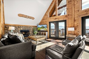 A cozy living room with a fireplace, stone wall, wooden ceiling, and a large window overlooking a scenic view. - Convenient Location*Views of Pigeon Forge*Two King Suites (PIGEON FORGE)
