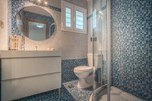 Une salle de bain avec un sol carrelé, des toilettes, un lavabo avec un miroir et un espace douche.