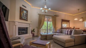 A living room with a fireplace, sofa, armchair, and a table with a vase. - Eleonas Private Pool Villa (Artemisia)