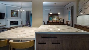 A modern kitchen with a marble island, wooden cabinets, and a dining area with chairs and a table. - Eleonas Private Pool Villa (Artemisia)
