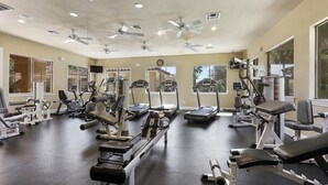 Een sportschool met diverse fitnessapparaten, plafondventilatoren en grote ramen.
