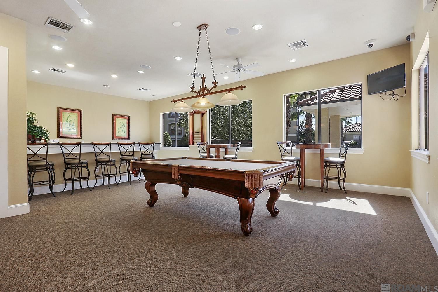 A pool table in a room with multiple chairs, a ceiling fan, and a large window.