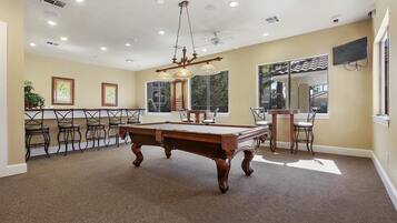 A pool table in a room with multiple chairs, a ceiling fan, and a large window.