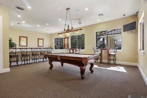 A pool table in a room with multiple chairs, a ceiling fan, and a large window.