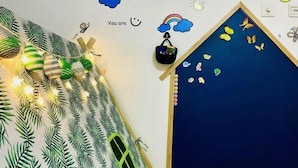 Una habitación con una pared decorada con motivos de hojas de palma, un pequeño estante con una cesta, y una pared azul con diseños de mariposas.