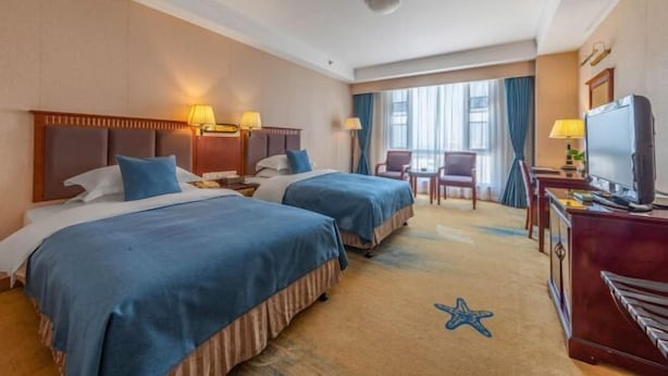 Habitación de hotel con dos camas, un escritorio, un televisor y una ventana con cortinas.