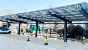 Un área de estacionamiento techada con paneles solares, un automóvil y conos de tráfico.