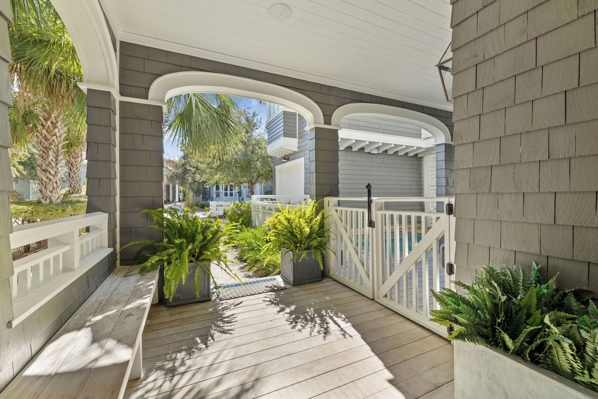 A covered porch with a wooden deck, white railings, and potted plants.
