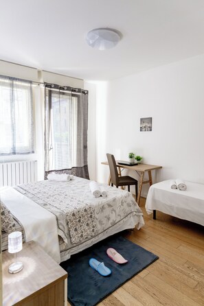 A hotel room with a bed, a desk, a chair, a small table with a plant, and a picture on the wall. - Charming Two Bedroom Private Apartment (Venezia)