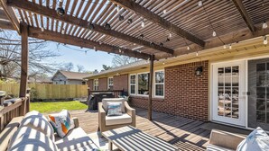 Un patio techado con mobiliario exterior, una parrilla y una casa de ladrillo al fondo.