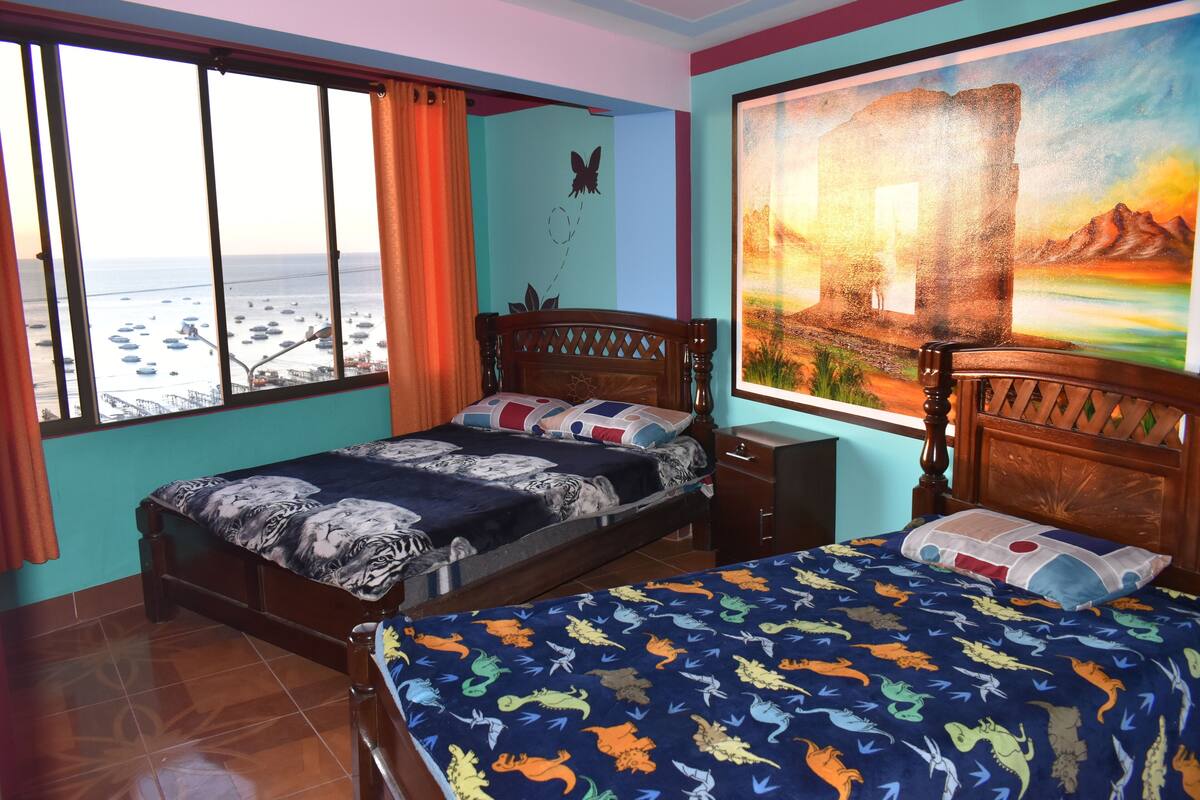 A bedroom with a bed, a nightstand, a window with curtains, and a painting on the wall.