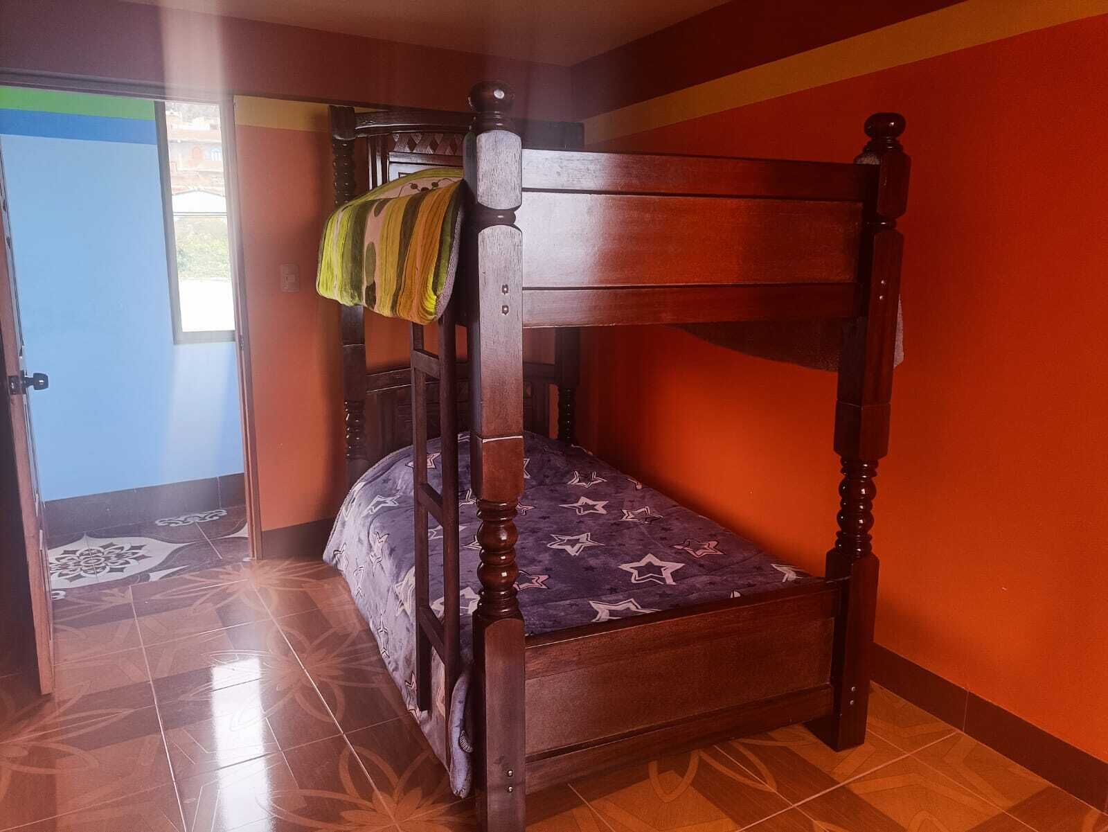 A wooden bunk bed with a patterned mattress in a room with orange walls and tiled flooring.