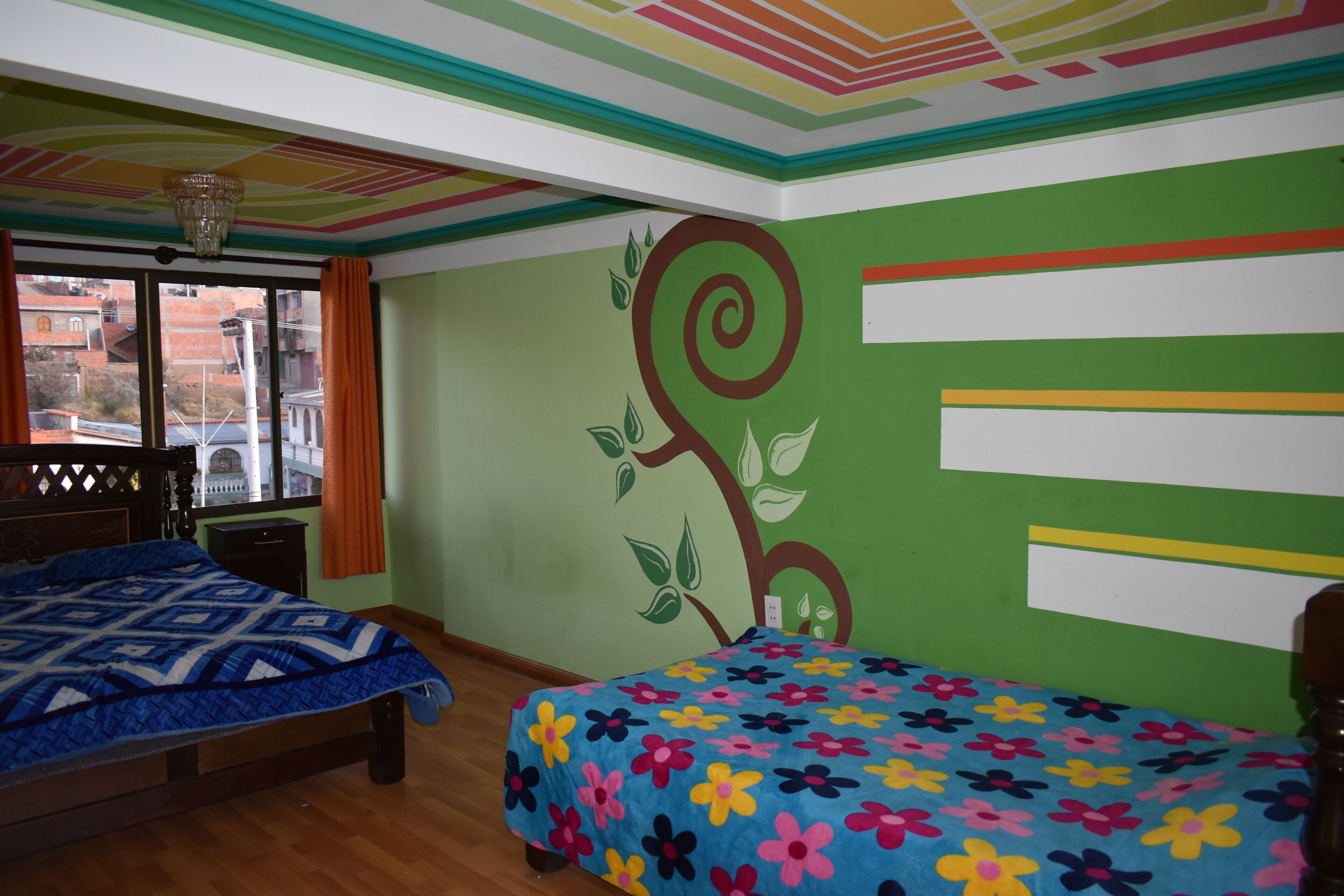 A room with two beds, a window with curtains, and a green wall with a floral design.