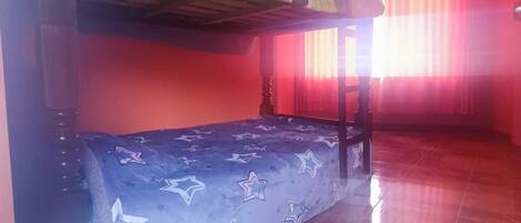 Una habitación con literas, ventilador de techo y ventana con cortinas.