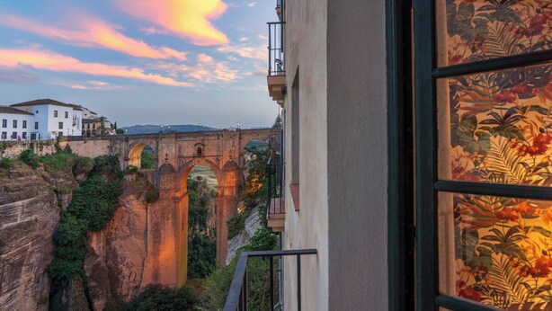 Vista desde un balcón con vista a un puente histórico y un río, con edificios al fondo.