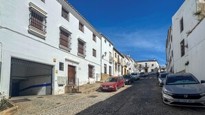 A cobblestone street lined with white buildings, parked cars, and a clear blue sky.