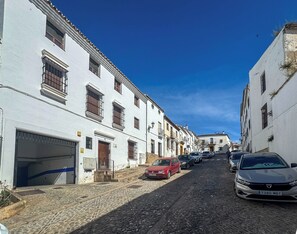 A cobblestone street lined with white buildings, parked cars, and a clear blue sky.