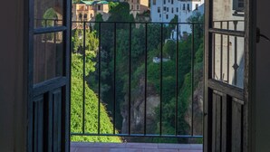 Puerta abierta que da a un balcón con vistas a edificios y vegetación.