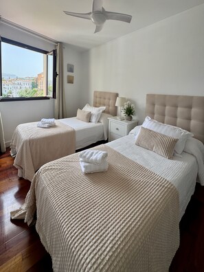 A hotel room with two beds, a ceiling fan, a nightstand with a lamp, and a window with a city view. - Las Vistas Residence - Best Views in Ronda (Ronda)