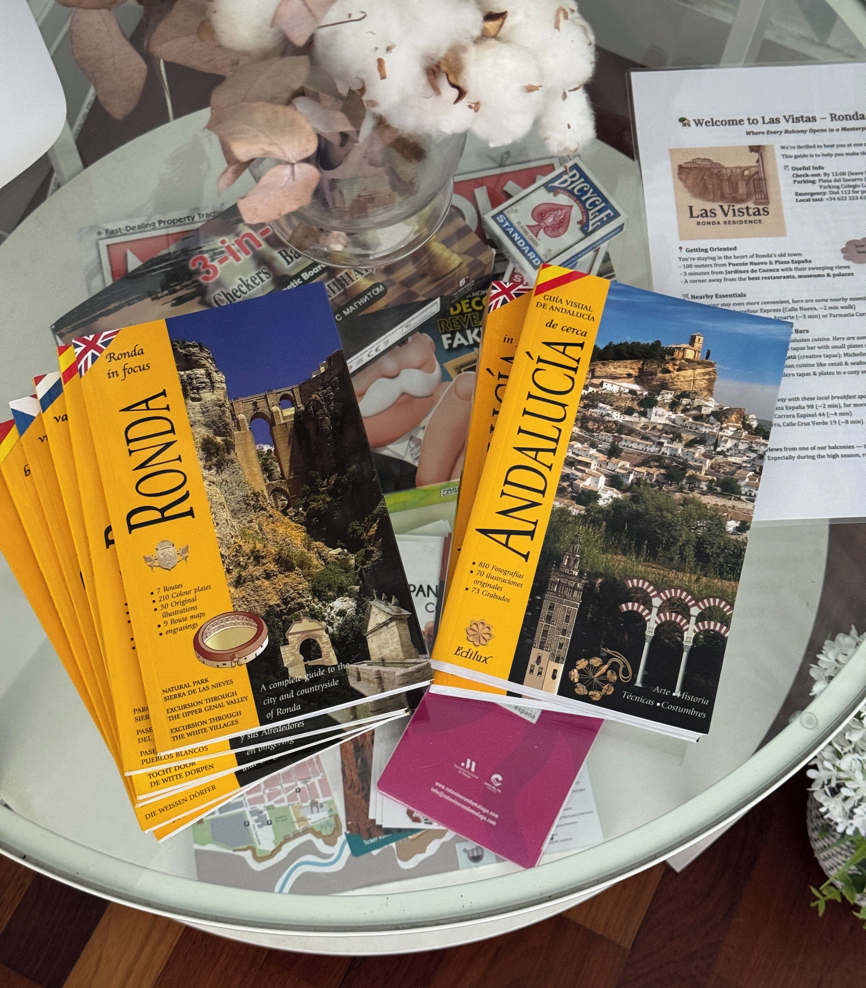 Une table avec des guides de voyage sur Ronda et l’Andalousie, un vase en verre contenant du coton, et une brochure posée sur la table.