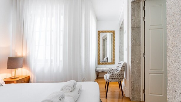 A hotel room with a bed, a chair, a desk, a mirror, and a door. - GuestReady - Lovely heaven in Porto (Porto)