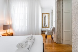 A hotel room with a bed, a chair, a desk, a mirror, and a door.
