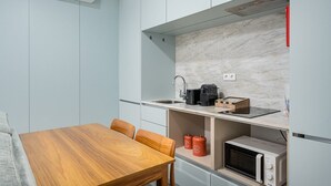 A compact kitchen with a wooden table, chairs, a sink, a coffee maker, a microwave, and two red containers. - GuestReady - Lovely heaven in Porto (Porto)