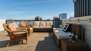 En tagterrasse med fletmøbler, en sofa og et lille bord med vinglas og en vinflaske.