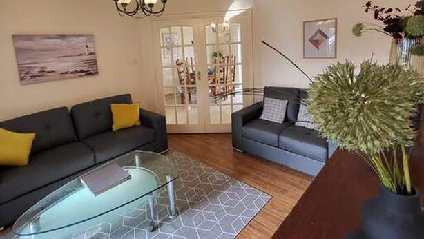 A living room with two sofas, a glass coffee table, a wooden floor, a chandelier, and a door leading to another room. - Mulberry House - Modern Family Retreat (Sligo)