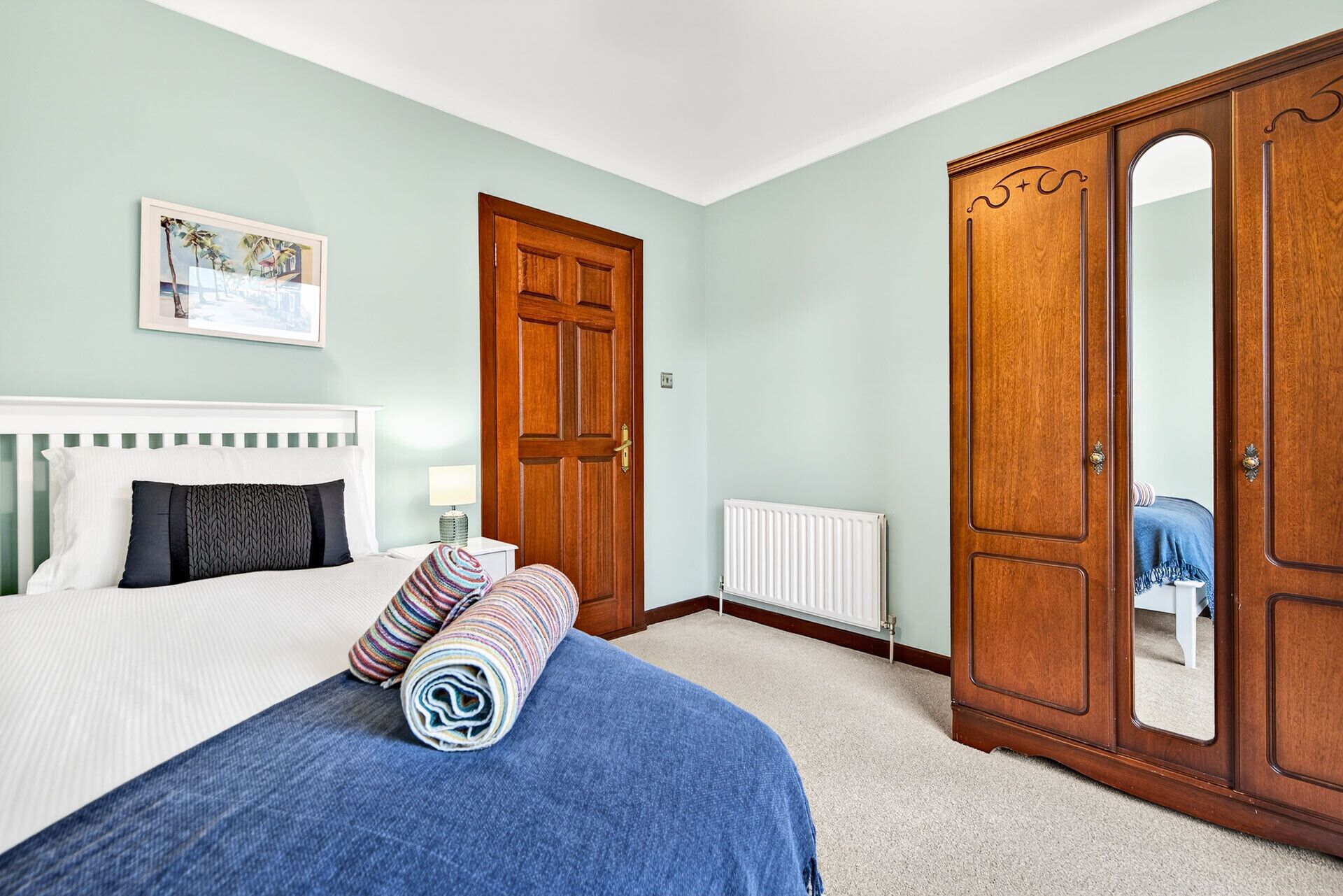 Une chambre à coucher avec un lit, une armoire en bois, un radiateur et un tableau encadré au mur.