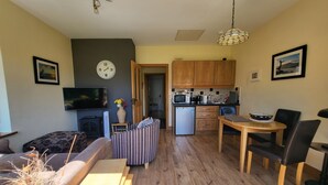 Un espacio habitable compacto con sofá, una pequeña mesa de comedor, una zona de cocina con armarios de madera, microondas y refrigerador.