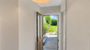Un passadís amb una làmpada de fusta al sostre, un estri d'entrada negre i vista a un jardí exterior.