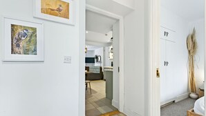 Passadís amb parets blanques, terra de fusta i una porta amb mànec de bronze. Hi ha obres d'art en marcs a les parets i es veu un indici d'una zona de menjador al fons.