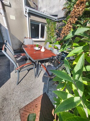 An outdoor patio with a wooden table and metal chairs, surrounded by greenery and a stone wall. - Wolfe Tone (Sligo)