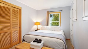 Quarto de hotel com cama, mesa de cabeceira, abajur, janela com cortinas, guarda-roupa e um pequeno banco com toalhas.