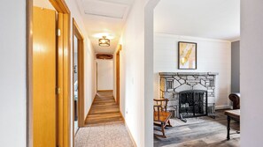 A hallway with wooden doors, a staircase, a fireplace with stone surround, and a framed picture on the wall.