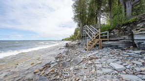 A rocky shoreline with a wooden staircase leading up to a platform. - Lakefront Escape | Fire Pit, Pets & Scenic Views (Sturgeon Bay)