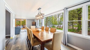 A dining area with a large wooden table, six chairs, and a chandelier. - Lakefront Escape | Fire Pit, Pets & Scenic Views (Sturgeon Bay)