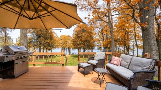 A deck with a grill, outdoor furniture, and a view of a lake surrounded by trees. - Lakefront Escape | Fire Pit, Pets & Scenic Views (Sturgeon Bay)