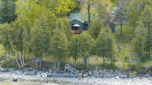 A cabin surrounded by dense forest, with a visible deck and a staircase leading to the entrance. - Lakefront Escape | Fire Pit, Pets & Scenic Views (Sturgeon Bay)