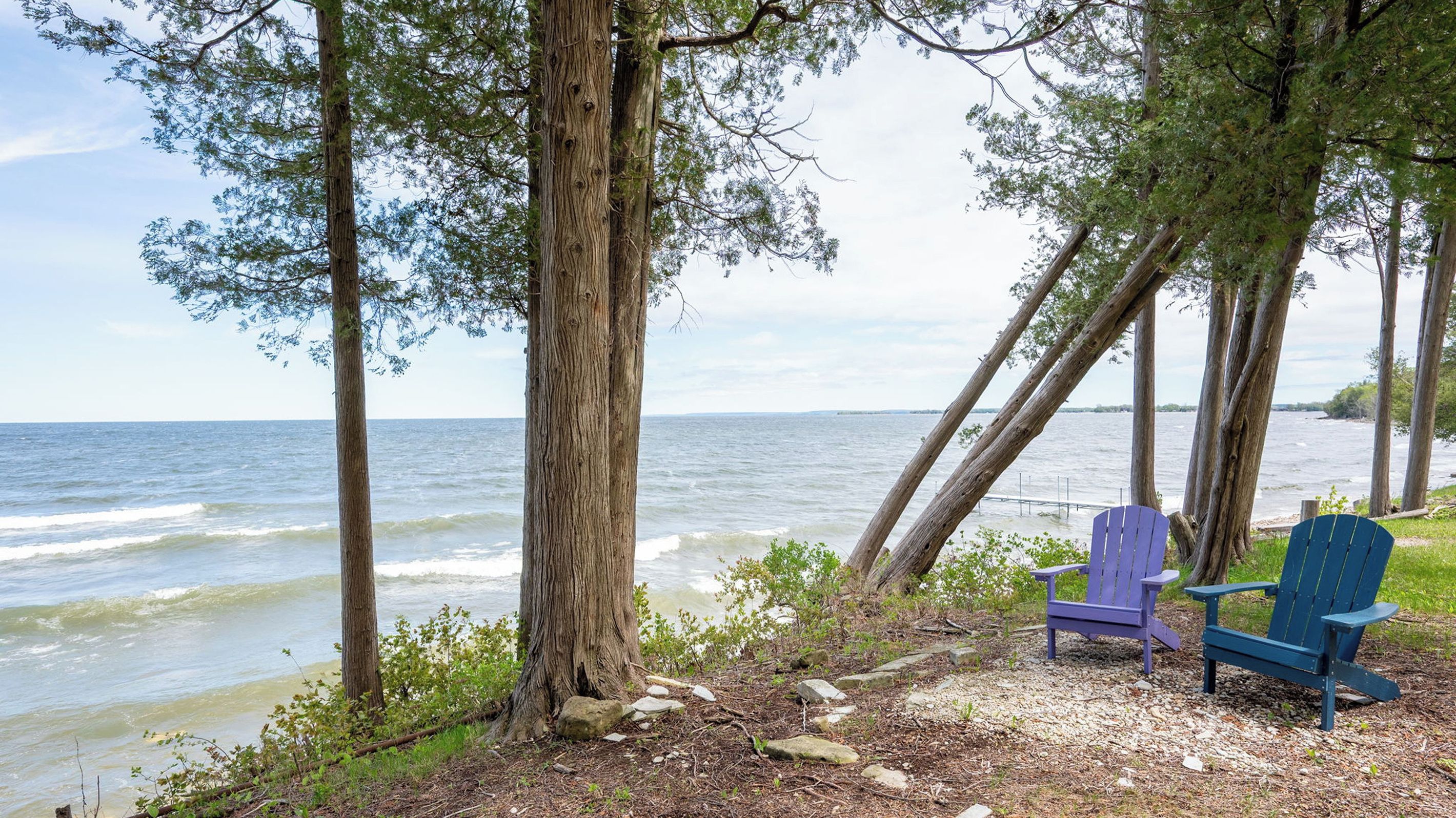 A beach with two Adirondack chairs, a rocky shoreline, and a view of the ocean.