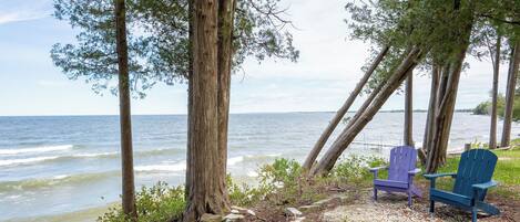 A beach with two Adirondack chairs, a rocky shoreline, and a view of the ocean.