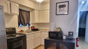A kitchen with white cabinets, a black stove, a microwave, and a coffee maker on a small table. - Large parking lot/sleeps 8 (Laredo)