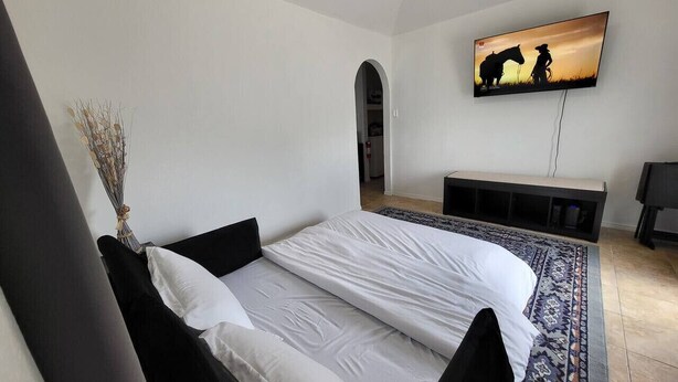 A bedroom with a bed, a TV on the wall, and a small desk. - Large parking lot/sleeps 8 (Laredo)